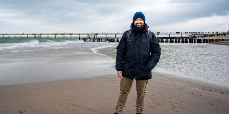 Dr. Wjahat Waraich steht in Winterjacke am Ostseestrand vor der Seebrücke.