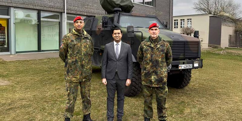 Dr. Wjahat Waraich steht zwischen zwei Feldjägern mit roten Baretten vor einem Militärfahrzeug.