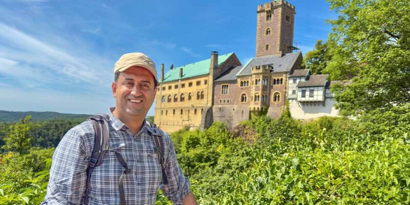 Dr. Wjahat Waraich steht mit Rucksack vor der Wartburg.