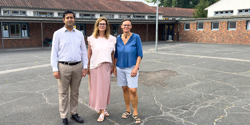 Dr. Wjahat Waraich steht mit zwei Lehrerinnen auf dem Schulhof der Grundschule Grimsehlweg.