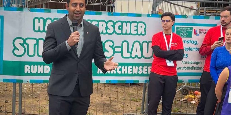 Dr. Wjahat Waraich spricht mit Mikrofon vor dem Banner des Hannoverschen Stiftungslaufs.