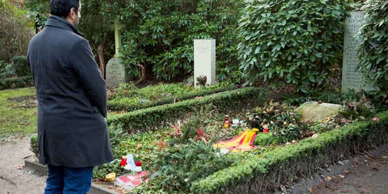 Dr. Wjahat Waraich steht am Grab von Helmut Schmidt, darauf Blumen und Kerzen.
