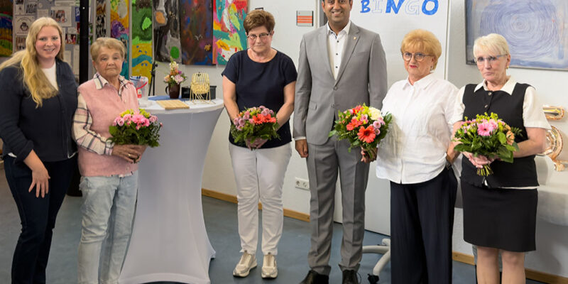 Dr. Wjahat Waraich steht mit den geehrten Ehrenamtlichen des NachbarschaftsCafés Sahlkamp, alle mit Blumensträußen.