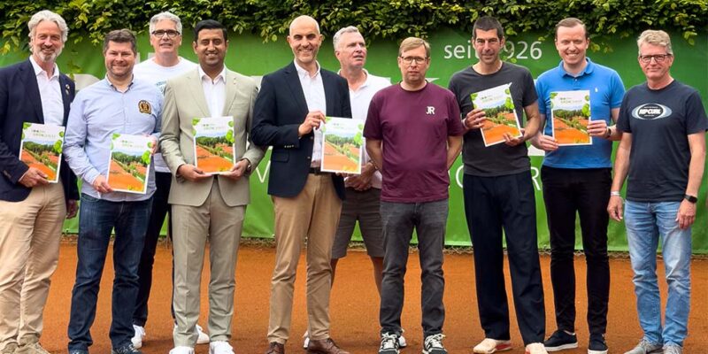 Dr. Wjahat Waraich steht mit Vereinsmitgliedern auf dem Tennisplatz zum 100-jährigen Bestehen von Grün-Weiss Hannover.