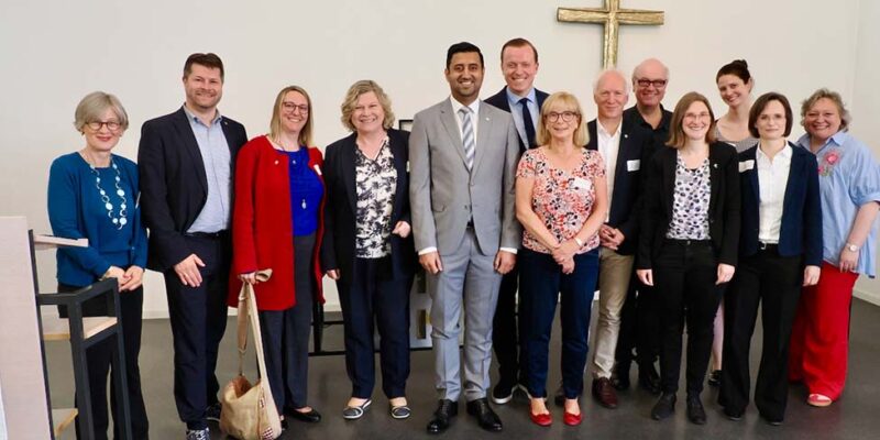 Gäste des achten ökumenischen Trinitatisempfangs stehen mit Dr. Wjahat Waraich vor dem Altarkreuz.