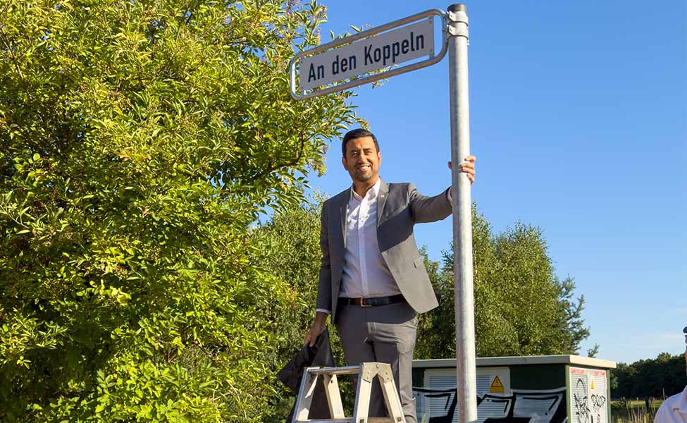 Dr. Wjahat Waraich steht auf einer Leiter und bringt das neue Straßenschild „An den Koppeln“ an.