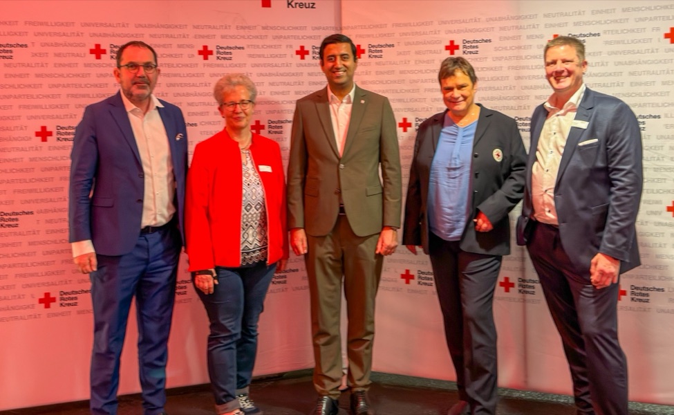 Dr. Wjahat Waraich steht mit vier weiteren Personen vor einer Stellwand des Deutschen Roten Kreuzes.
